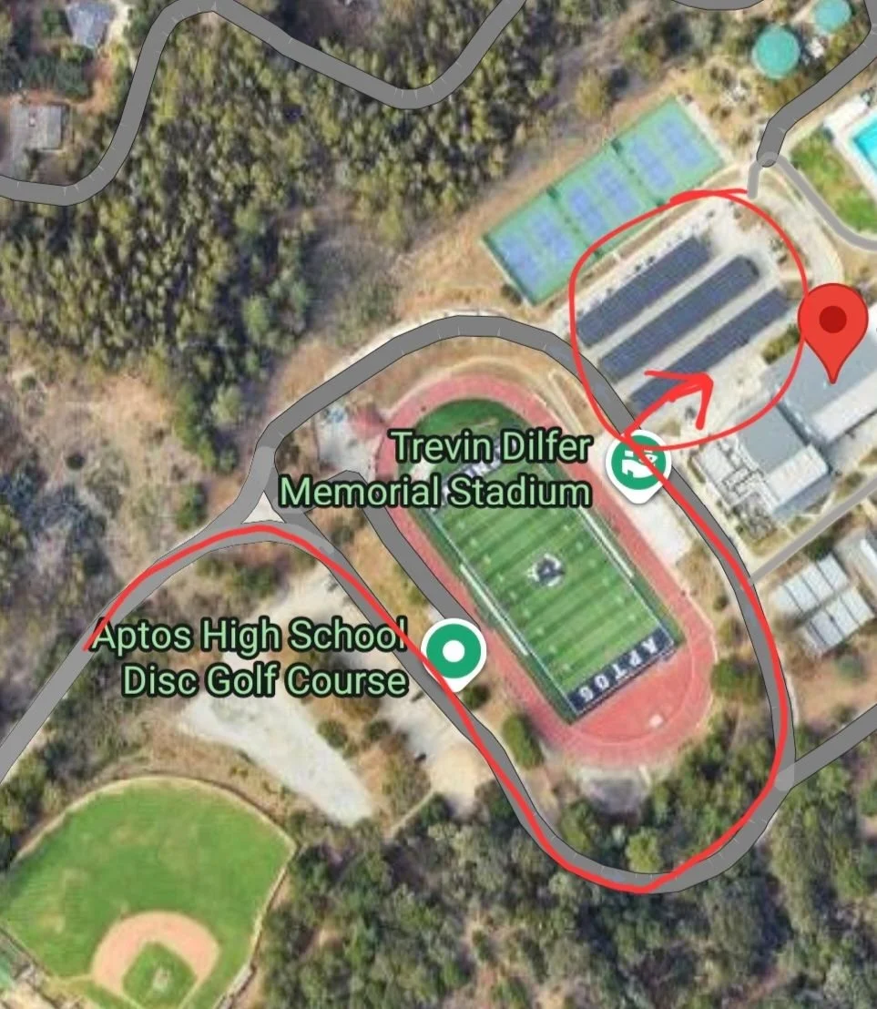 Satellite map of the school campus. A red line follows the campus road around the football stadium to the parking lot with solar-panel carports, circled in red beside the Main Gym, which the red map pin marks.