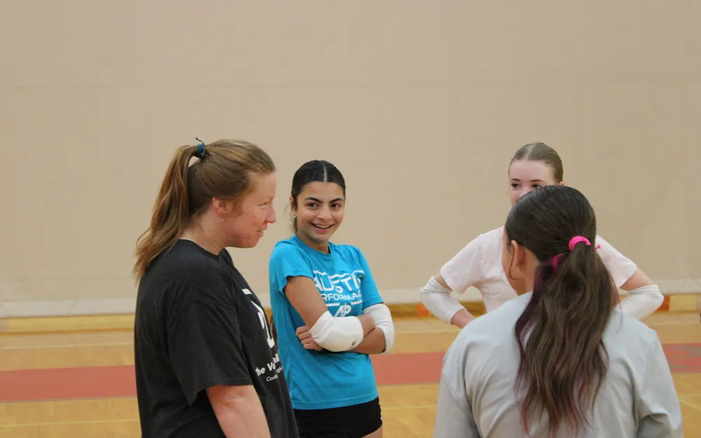 A TVI Trainer laughing with three young athletes standing together between drills in a gym