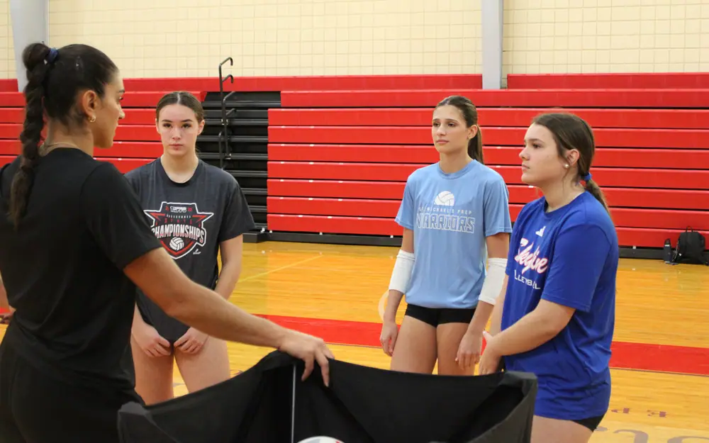 Juliann Faucette, a TVI Trainer, at a ball cart talking with three athletes lined up in front of her