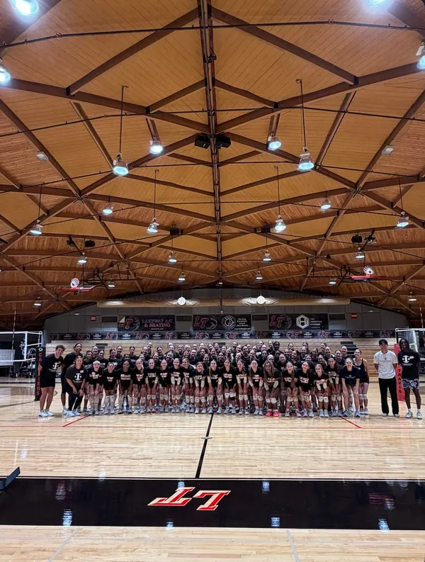 About a hundred high school athletes and TVI Trainers together on the court under a wood-beam gym ceiling at a Team Camp