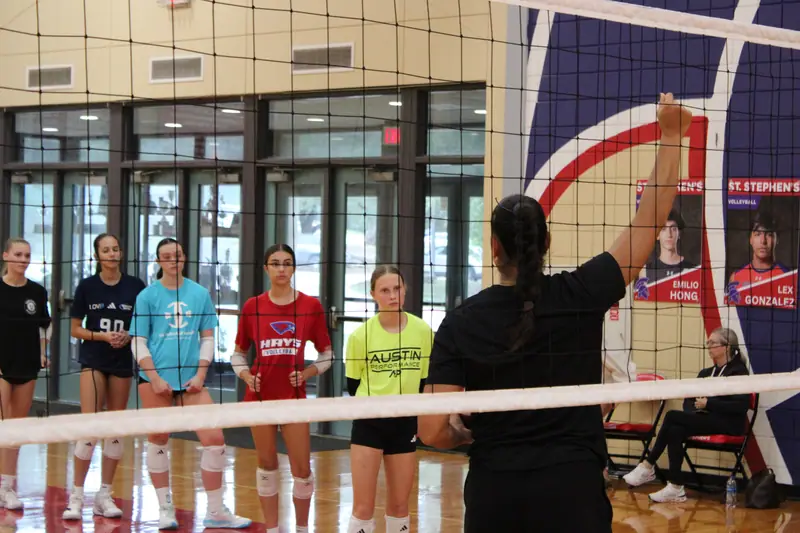 Juliann Faucette, a TVI Trainer, at the net with her arm raised, leading a lineup of athletes through a drill